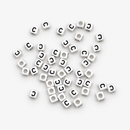 A pile of small white cube-shaped beads with a black letter 'C' printed on one side, scattered on a plain white background.