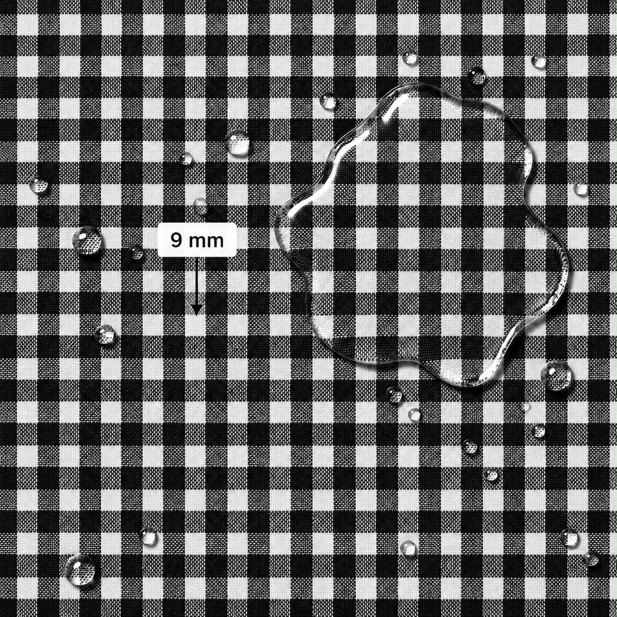Black and white gingham fabric surface with scattered water droplets and a larger irregular droplet, plus a label reading 9 mm indicating fabric scale