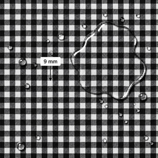 Black and white gingham fabric surface with scattered water droplets and a larger irregular droplet, plus a label reading 9 mm indicating fabric scale