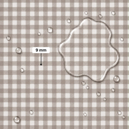 A close-up of a beige and white gingham fabric surface with scattered clear water droplets and a large transparent puddle of water on the right. A label reading '9 mm' with an arrow points to the puddle, indicating fabric scale