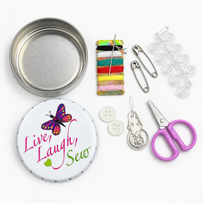 A sewing and pinning kit arranged on a white background, including a round metal tin, a white pin cushion with a butterfly and the words 'Live, Laugh, Sew,' thread spools, safety pins, clear plastic buttons, white buttons, lavender-handled scissors, and a metal pin pull.