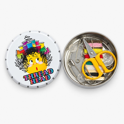A circular metal sewing tool tin shown open on a light gray background. The lid features a cartoon illustration of a yellow character with colorful thread spools on its head and the words 'THREAD HEAD'.