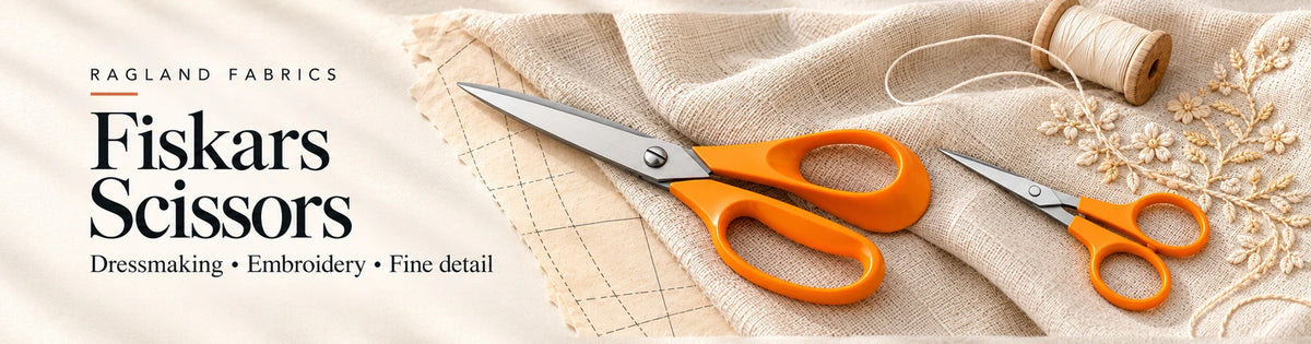 Ragland Fabrics Fiskars Scissors: orange-handled dressmaking and embroidery scissors on ivory linen with sewing pattern and fine stitchwork.